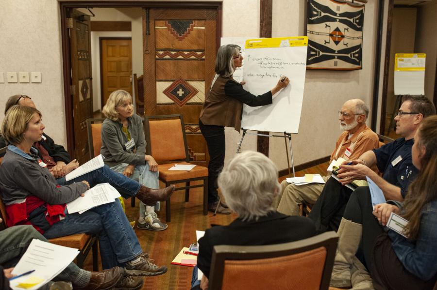 Community members sitting in a circle with one person writing on a flip chart in front of them.