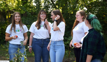 Young women in matching t shirts gather outside in a garden.