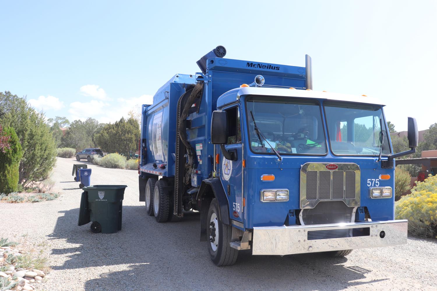 A blue recycling truck next to waste bins.