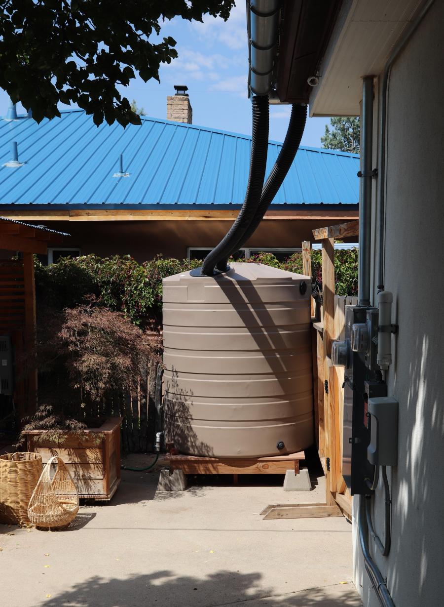 A large, tan rain barrel connected to the outside of a building.
