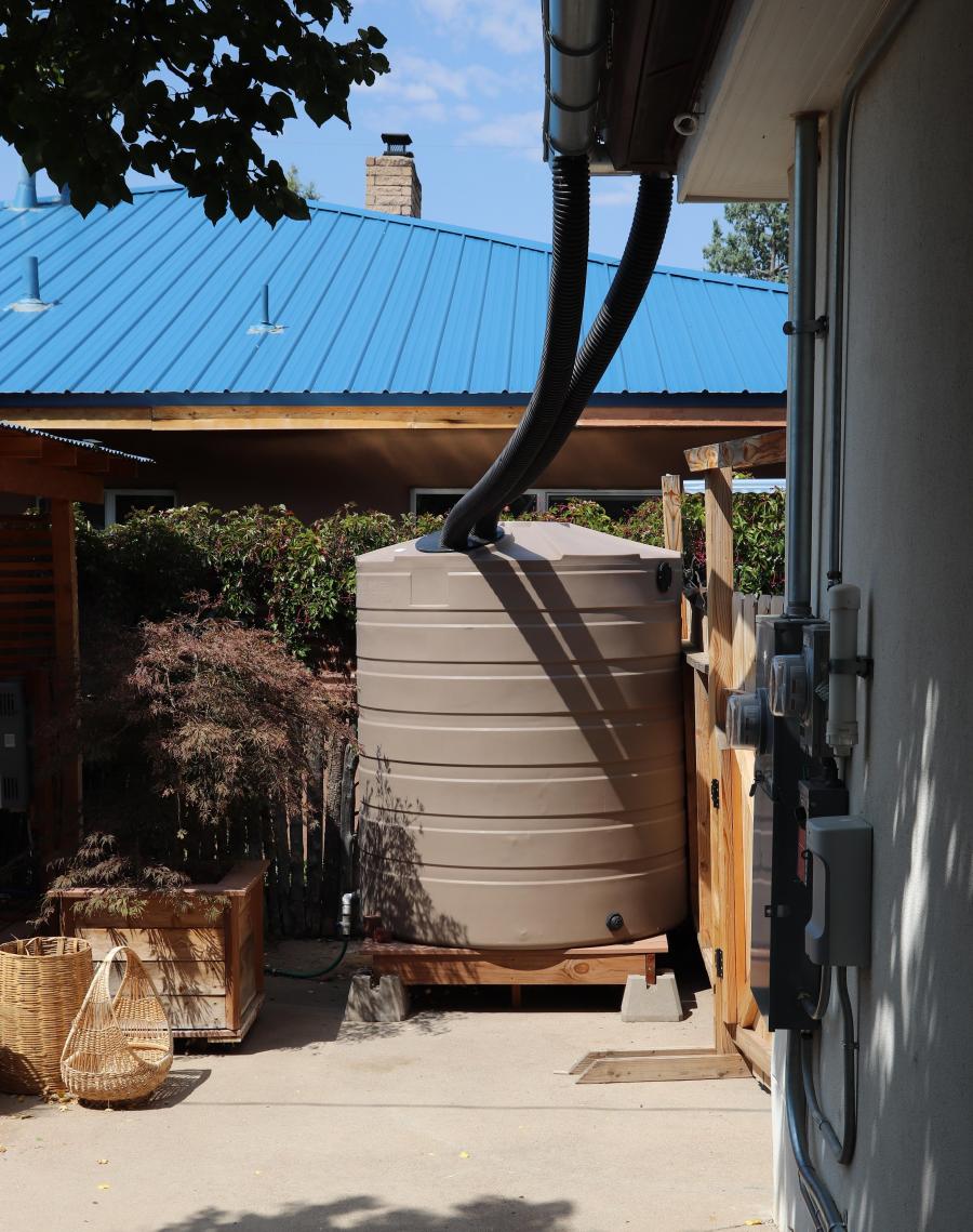 A large, tan rain barrel connected to the outside of a building.