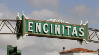 Green and white Encinitas city sign hangs over a street.