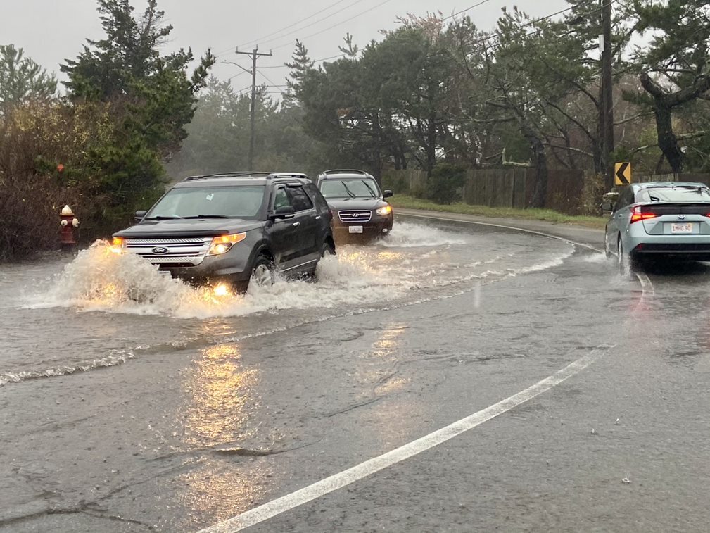 Two cars drive through water in a flooded street.