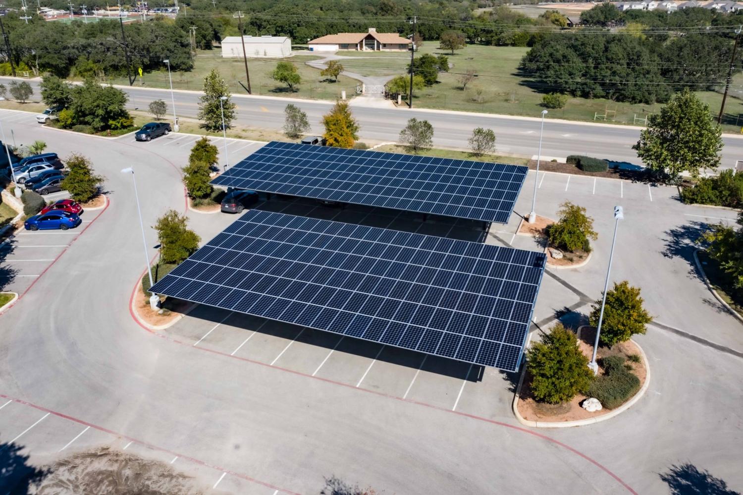 two large solar panel arrays in a parking lot with sparse trees