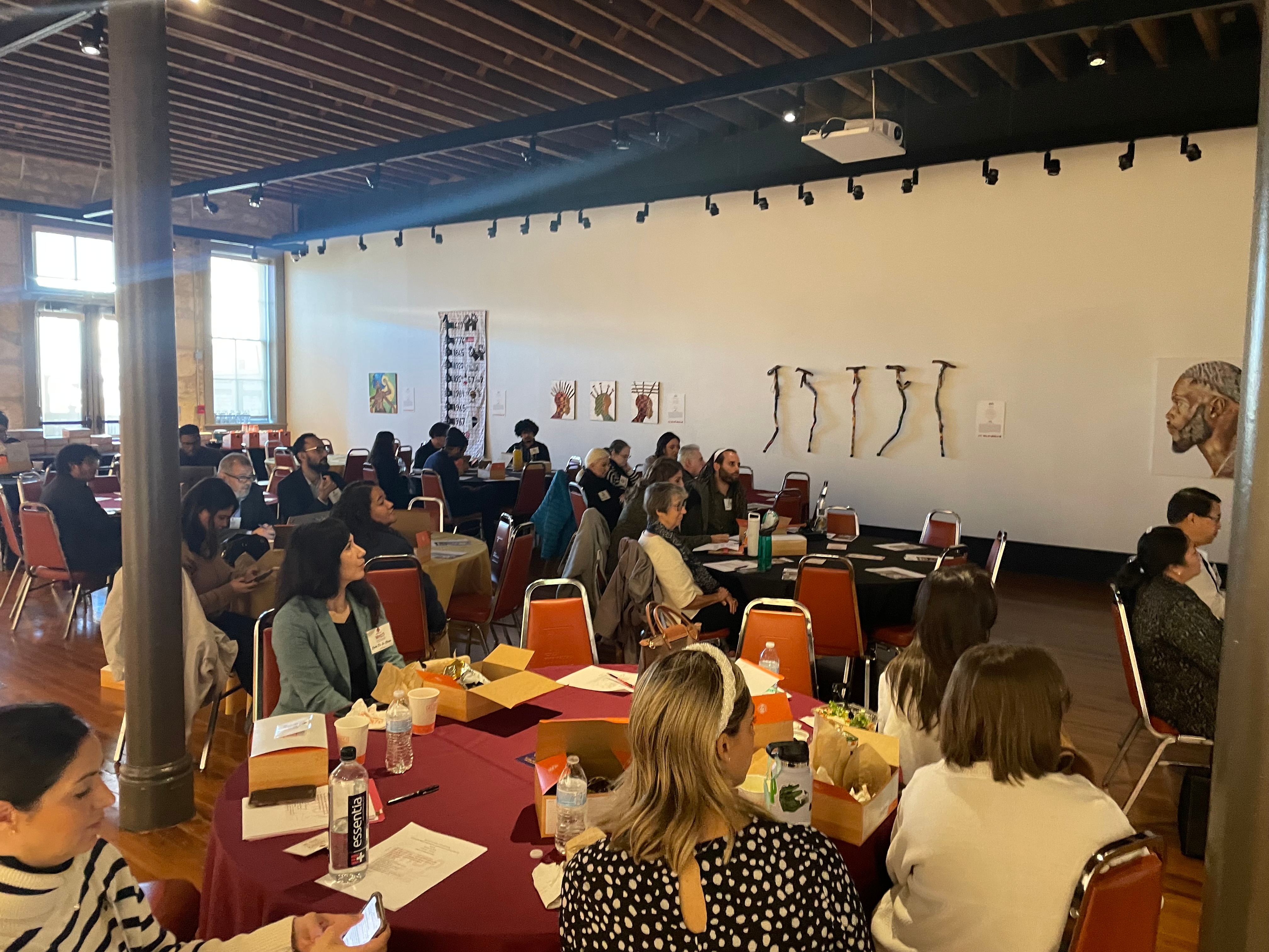 a wide shot of a room full of folks sitting at round tables looking toward the right side of the photo, likely at a presenter. 