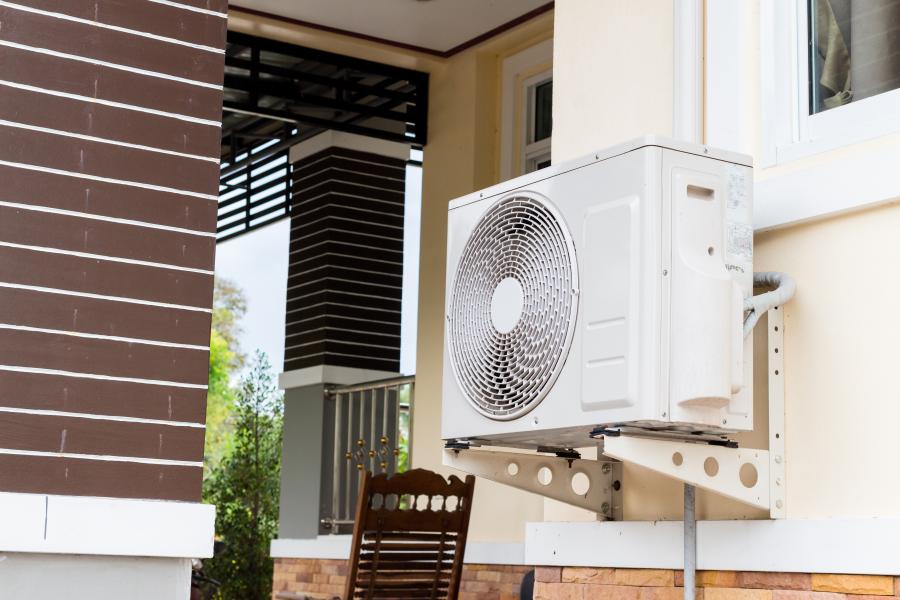 photo of a heat pump attached to the side of a building with a chair in the background