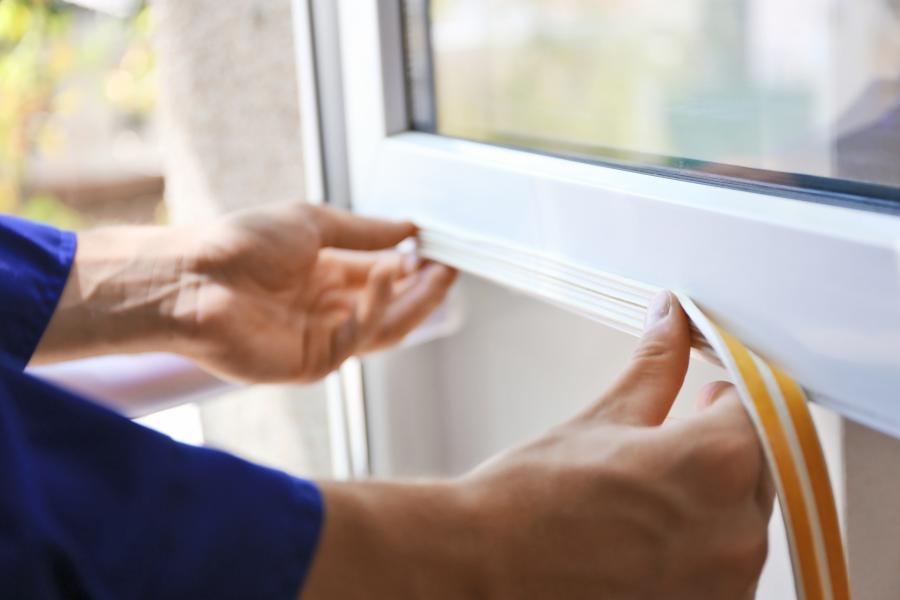 two hands pressing window sealant on a window to help weatherize it