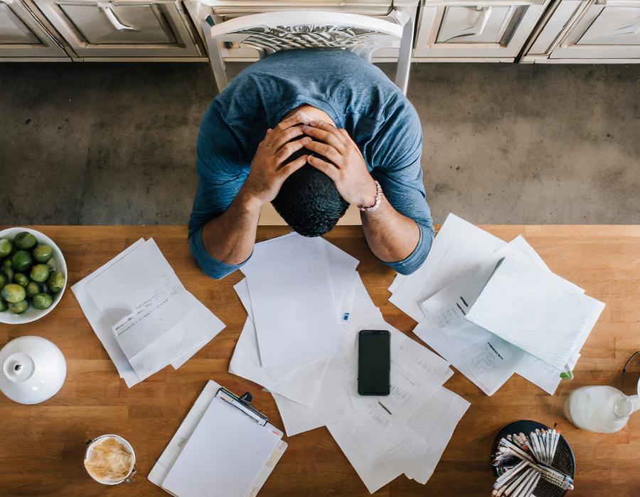 An overhead view of a man with his head down and a pile of scattered documents on his desk.