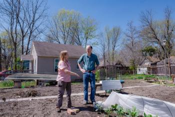 Two people talk while standing over home garden