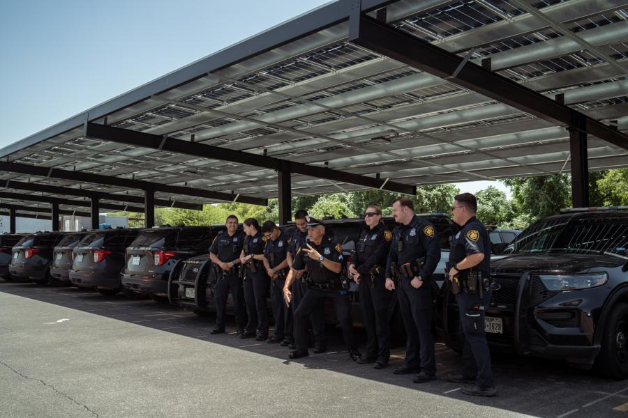 Photo of police officers posing in front of police vehicles parked under solar panels