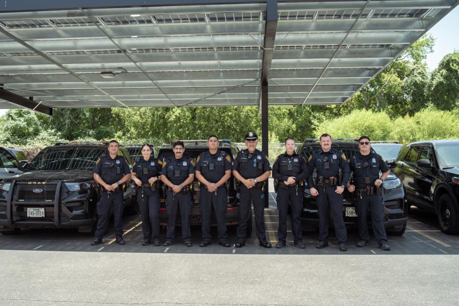 Photo of police officers posing in front of police vehicles parked under solar panels