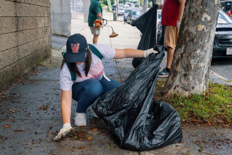 A woman picks up trash on the sidewalk