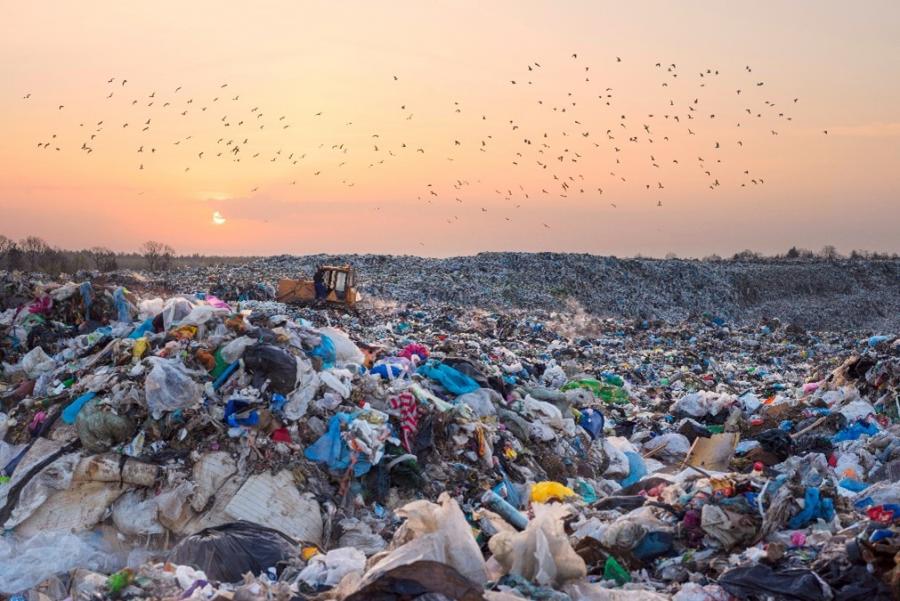 A bulldozer works in an active landfill with a sunset in the background