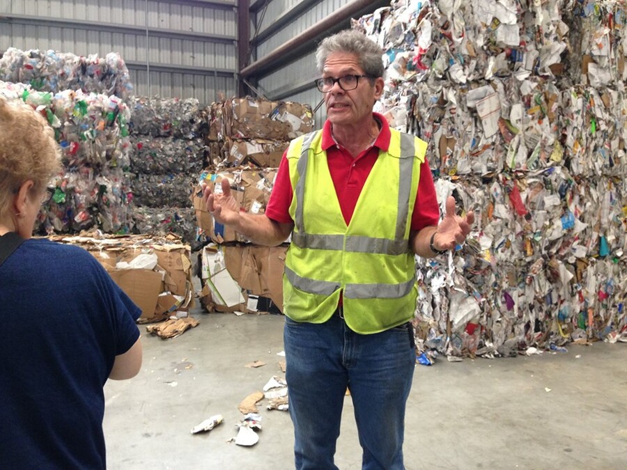 A man in a safety vest is explains recycling in front of bales of recyclable material