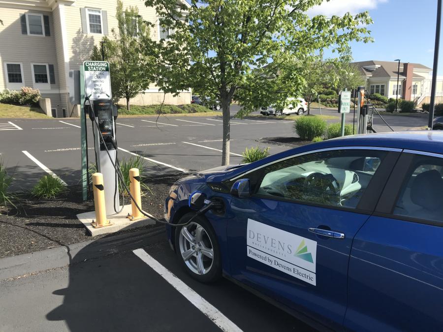 An electric vehicle is shown charging at a public charging station in Devens.
