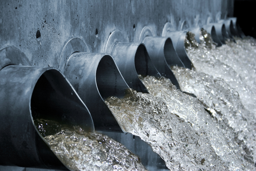 A photo of pipe many outlets from a concrete wall with a lot of water pouring out of them. 