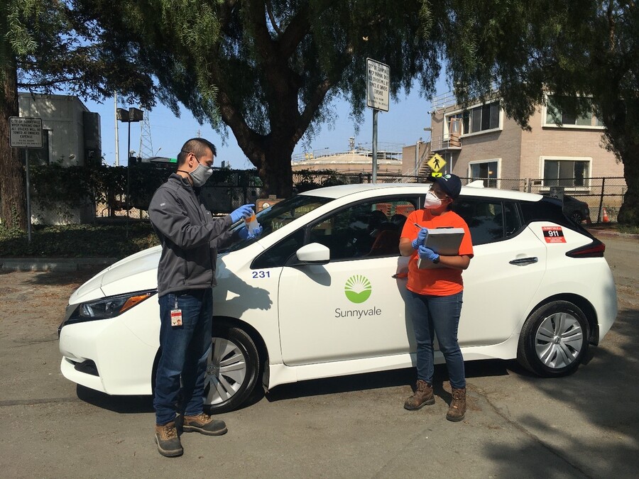 Photo of two people standing in front of a white electric vehicle with the Sunnyvale logo on the driver side door. 