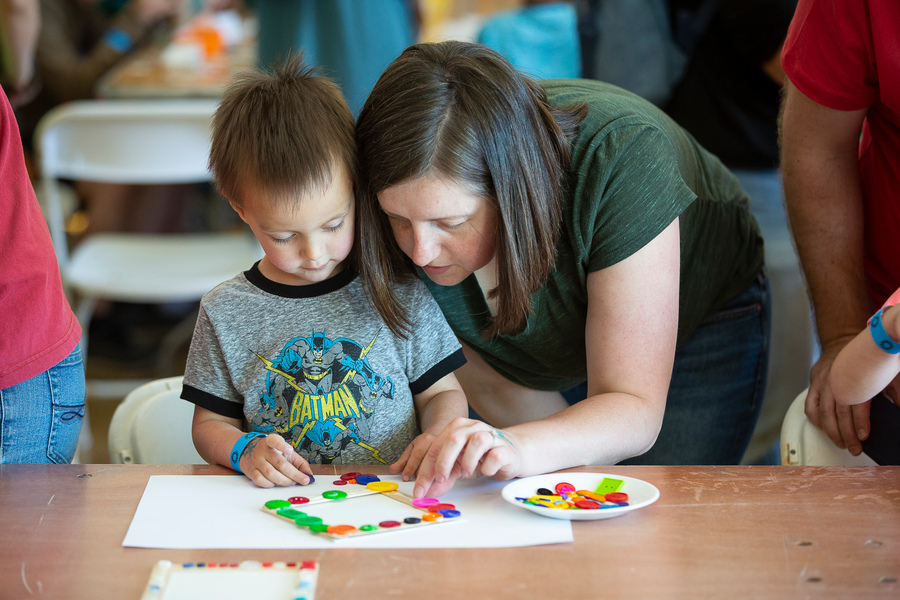 An adult leaning down and helping a child with an art project at a table