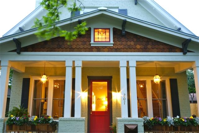 photo of the front porch of a home with a red front door and four lights on; 2 on each side of the door. 