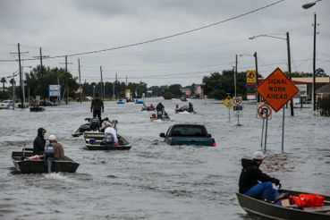 A flooded street with cars underwater and people in small boats along road signs