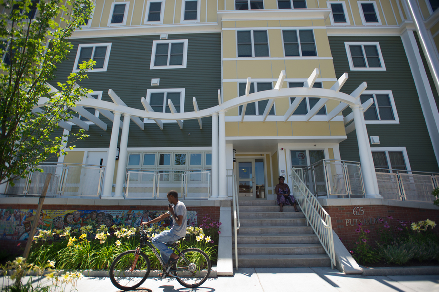 Front of a 4-story apartment building with street trees and cars parked along the street