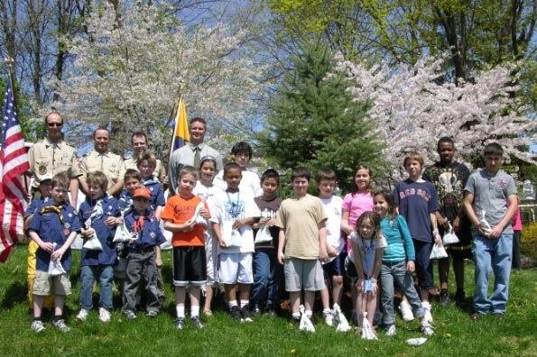 Group of young children and several Watertown Town staff pose for a picture in front of blossoming trees during Arbor Day in Watertown, Massachusetts.