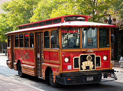 Red trolley with the words "Red Route" in the front window. Trees and stores are in the background