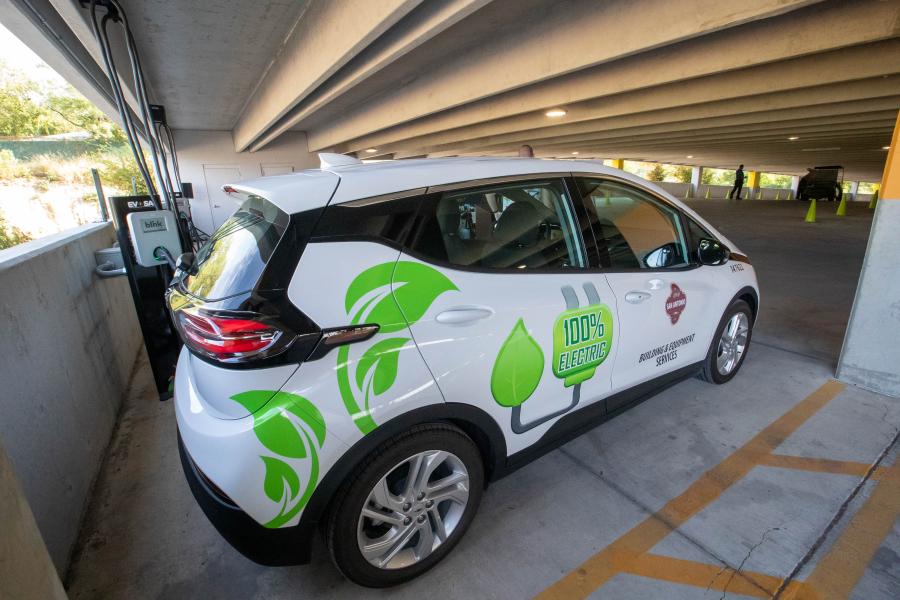 A photo of one of the City of San Antonio's electric vehicles used for municipal operations. The vehicle is white with green leaves and a green plug that says "100% Electric".