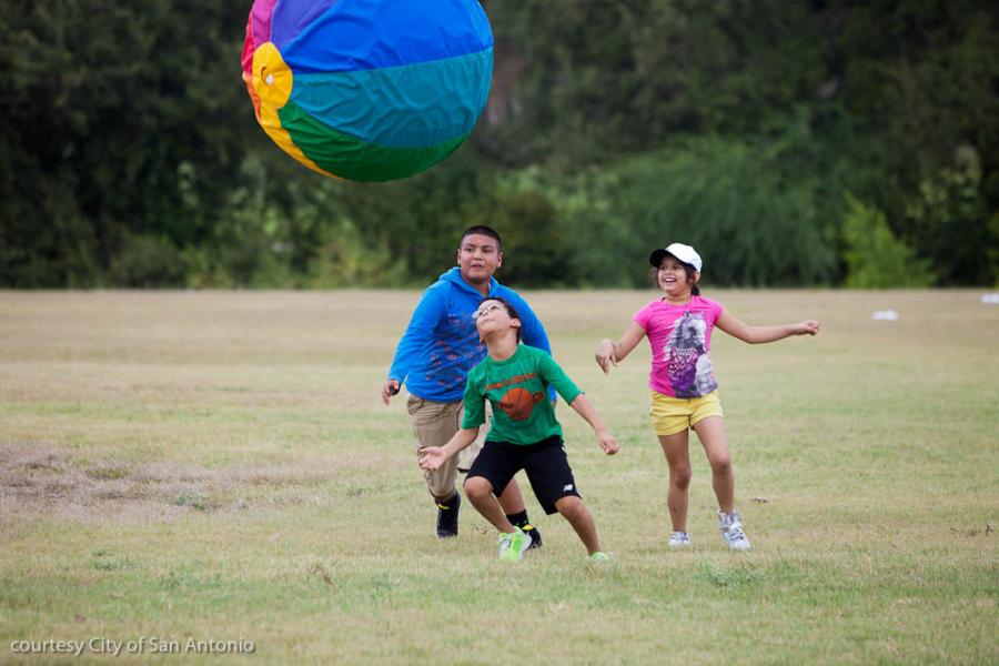 people playing in a field with a large multi colored ball suspended in the air above them