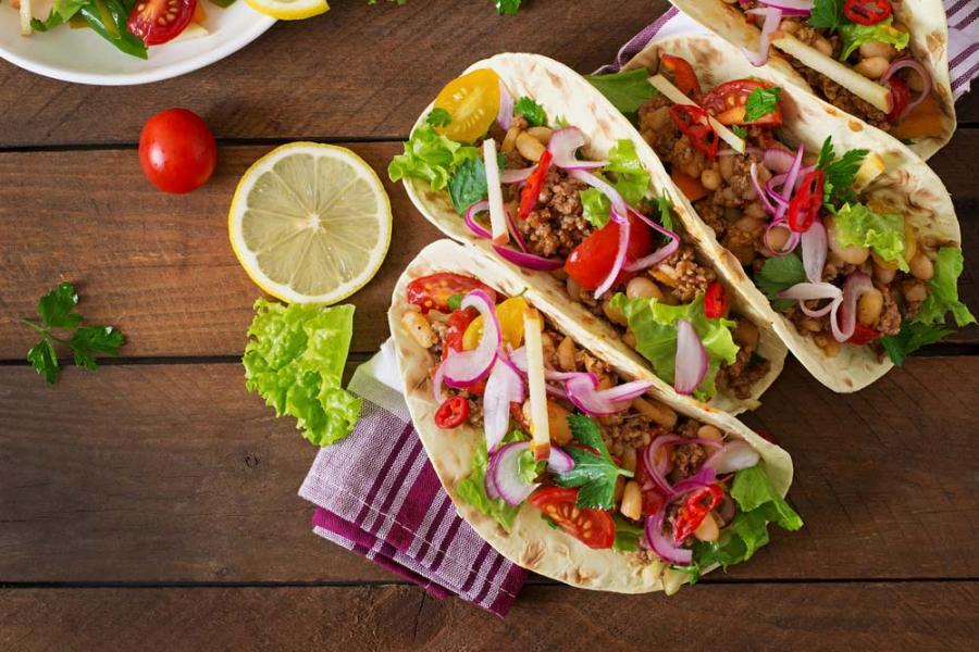 Photo of street tacos lined up on a towel on a wooden table