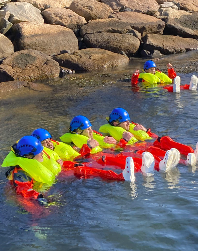 Four people in helmets and lifejackets float in shallow water during a safety training exersize.