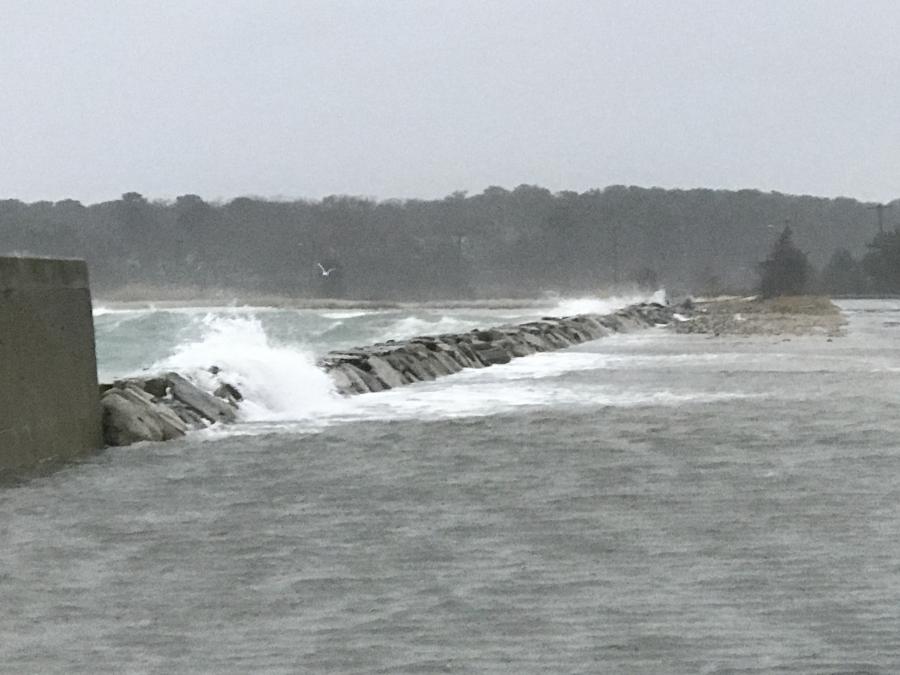 Large ocean waves crashing over a stone pier.