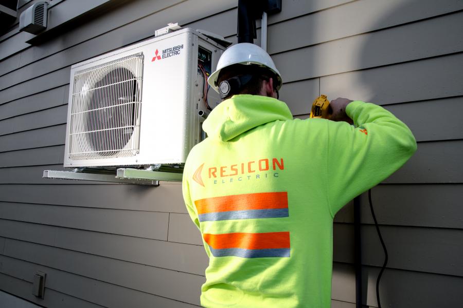 Man in neon sweatshirt and safety helmet installing a heat pump on the exterior of a home.