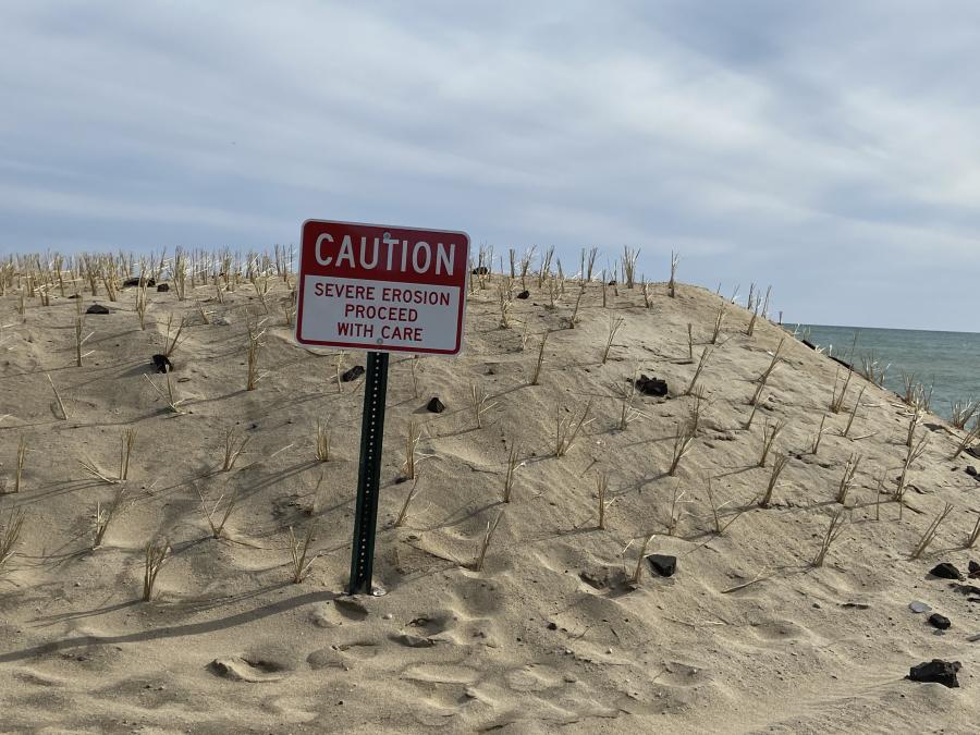 Caution sign in front of eroded beach area.