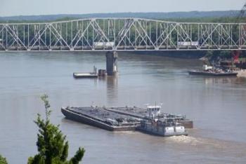 A barge moves up the Missouri river under a car bridge.