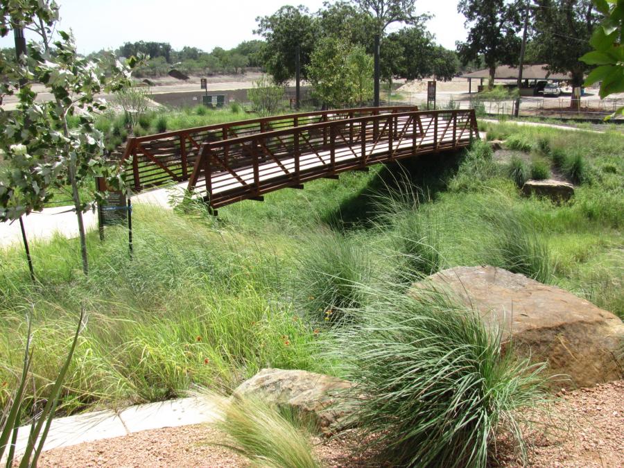 A landscaped walkway with a pedestrian bridge over a shallow ditch